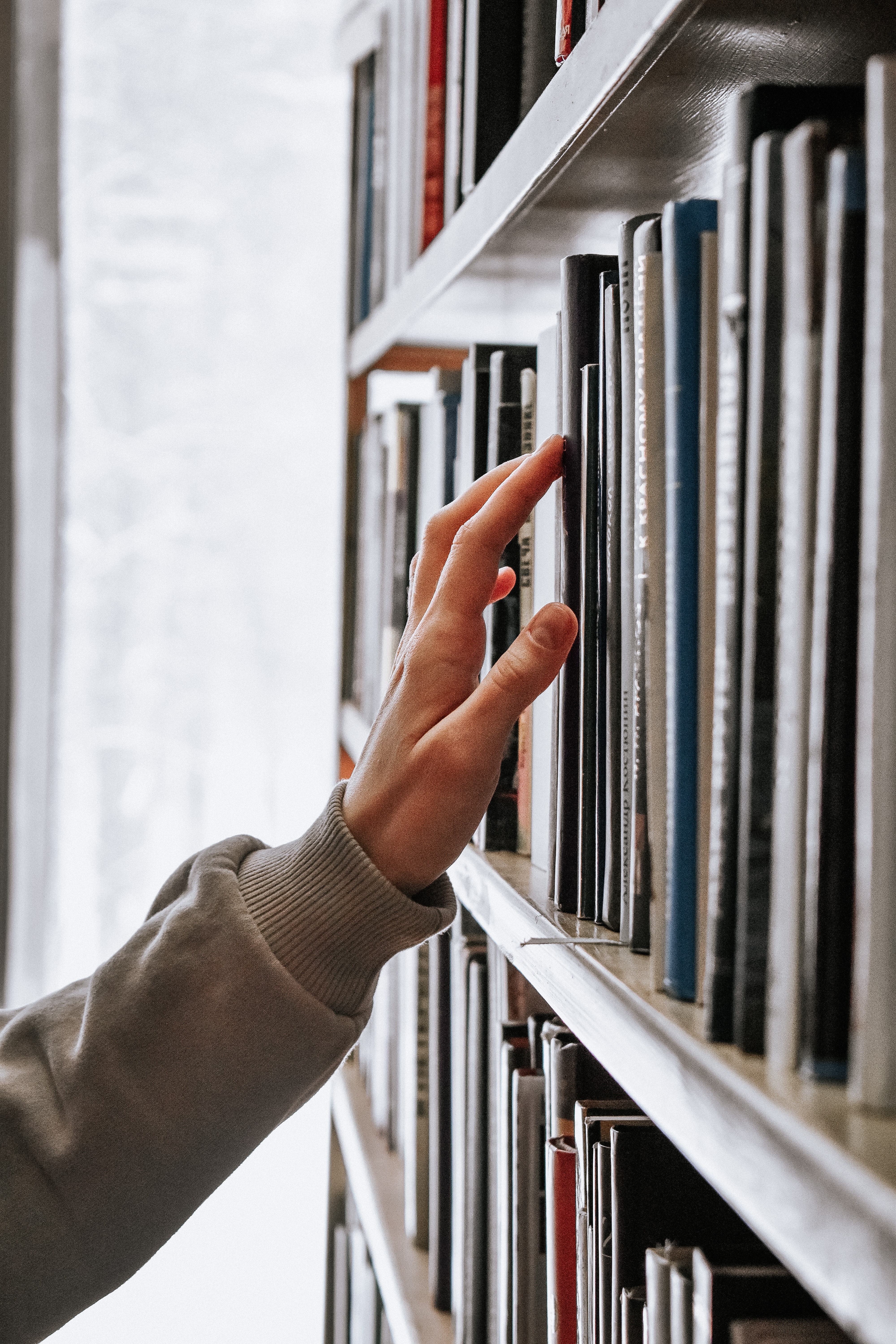 hand searching a book shelf.