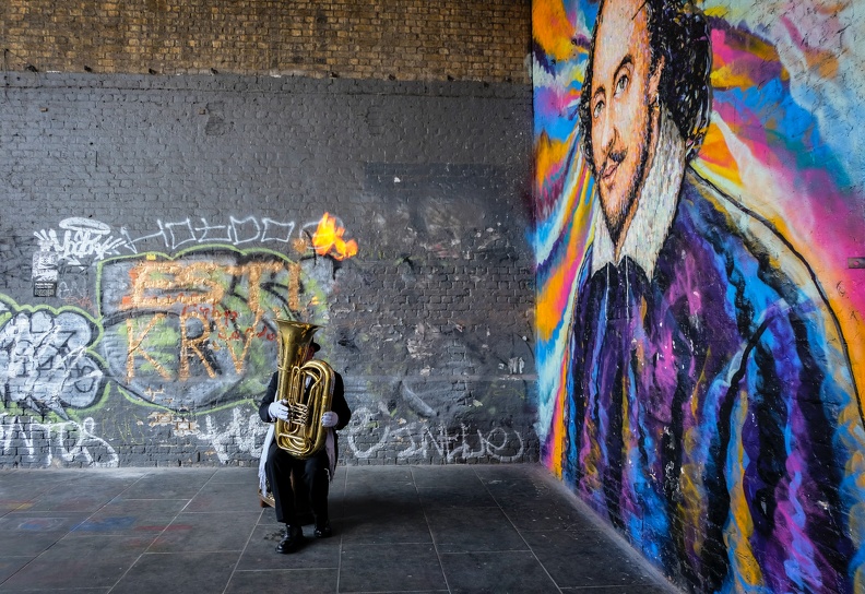 A tuba player in front of a Shakespeare mural.